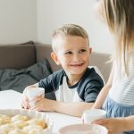 Smiling siblings sharing a breakfast table with milk and pastries in a cozy home setting.